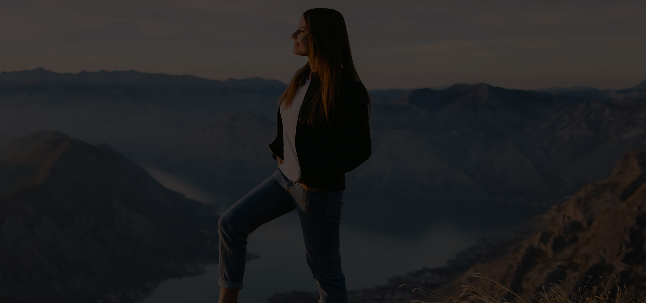 Person standing on mountain overlooking a lake.