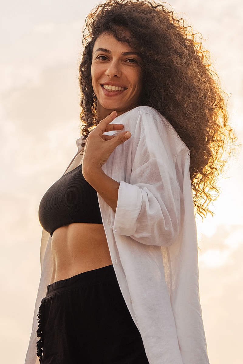 Smiling woman in casual beach attire at sunset.
