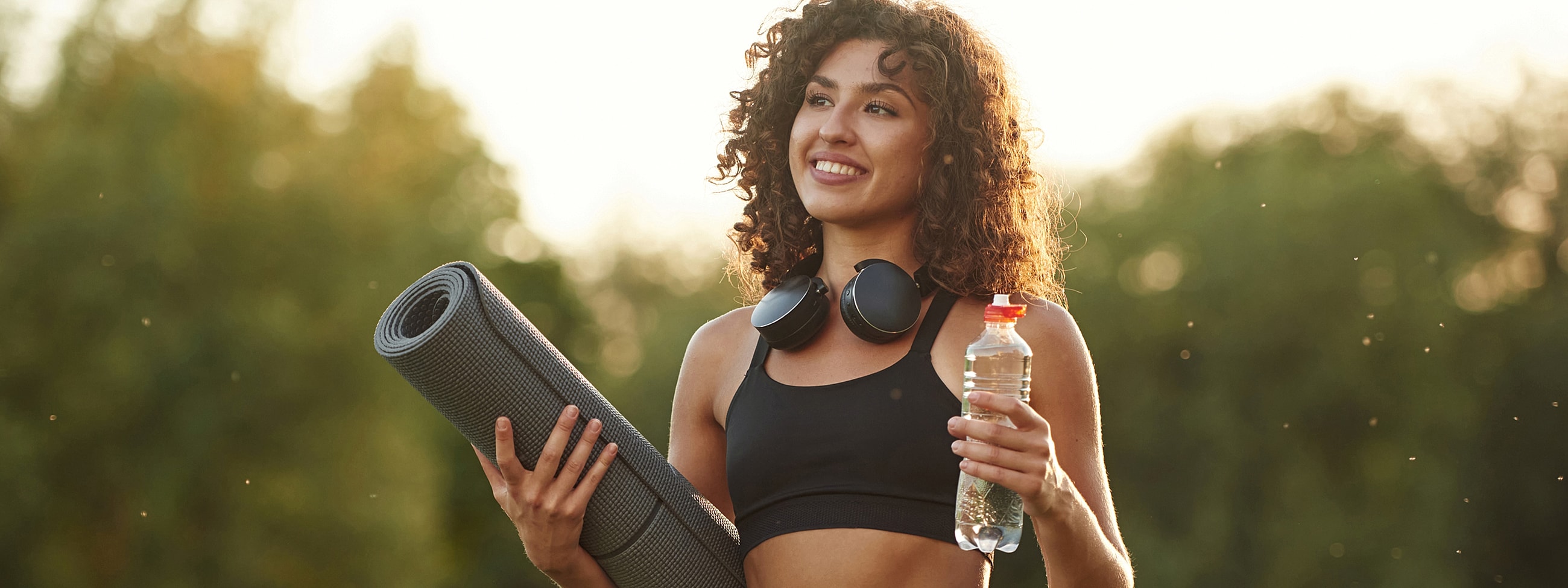 Woman with yoga mat and water bottle outdoors.