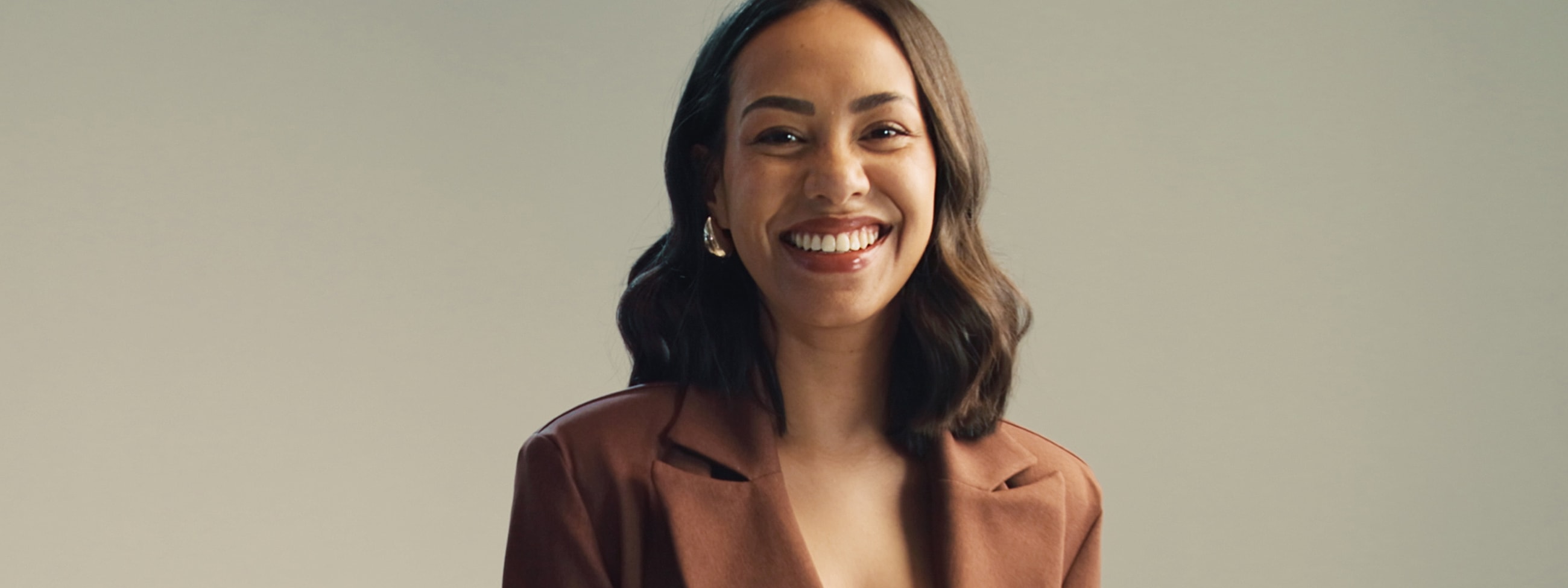 Smiling woman in a brown blazer against backdrop.